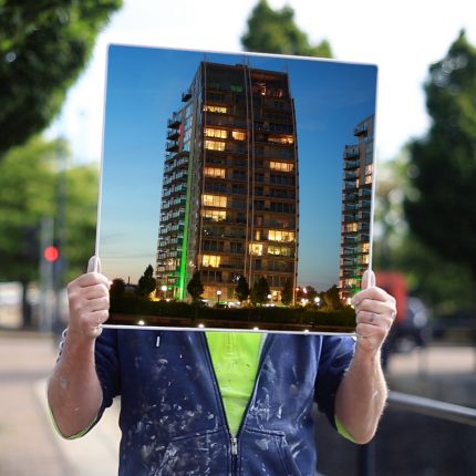 Man holding large photograph of a buidling in front of his face.