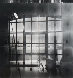 Black and white photograph of a window in the foreground and the view of industrial buildings in outside of the window.