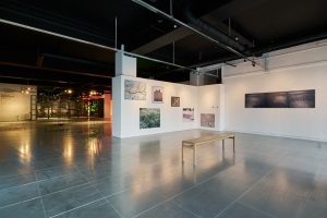 Photograph of gallery space. White walls with photographs on and a bench is positioned in the foreground.