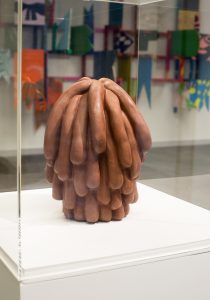 Terracotta sculpture in perspex display box. The sculpture looks like a pile of sausages.