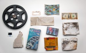 Photograph of what appears to be disregarded objects, including an American Dollar, a film reel, a photographic slide and a Queen concert ticket.