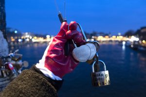A gloved hand holding two 'love locks' and a padlock.