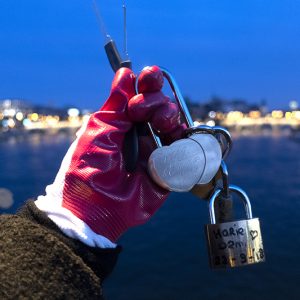 A gloved hand holding two 'love locks' and a padlock.