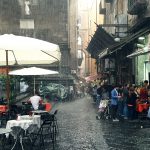 A rainy street scene in Naples, Italy, people are sheltering from the rain.