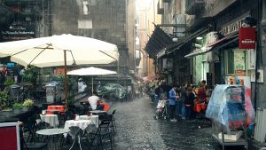 A rainy street scene in Naples, Italy, people are sheltering from the rain.