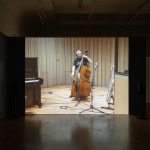A still from a video showing a white man in a recording studio playing a double bass