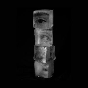 a contemporary artwork image. It shows a stack of 4 ice cubes against a solid black backgroun. Superimposed on or in the ice cubes are black and white images of human eyes and facial features