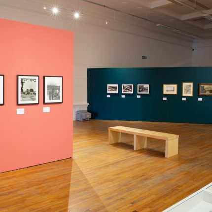Interior photo of a gallery exhibition. The image shows a pink wall and a green wall, with small framed artworks hung on them.