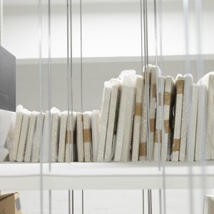 a set of small canvasses seen from the side. They are all wrapped up and placed side by side on a white shelf.