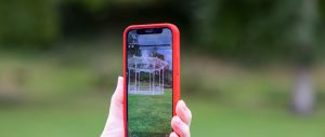 a hand holds up a smartphone, on the screen a digital image of a bandstand is superimposed on the background of a park