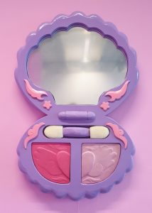 Stylised purple sculpture of a 2000s style make-up compact with mirror.