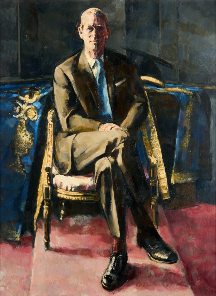 An oil painting depicts Prince Philip sitting with in a gold chair, facing the viewer, one leg crossed over the other, and his hands in his lap. He is wearing a brown suit with a blue tie.