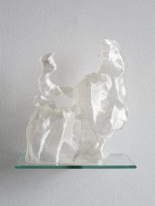 An abstracted 3D printed plastic sculpture with a white pearlescent finish, on a small glass shelf against a white background. 