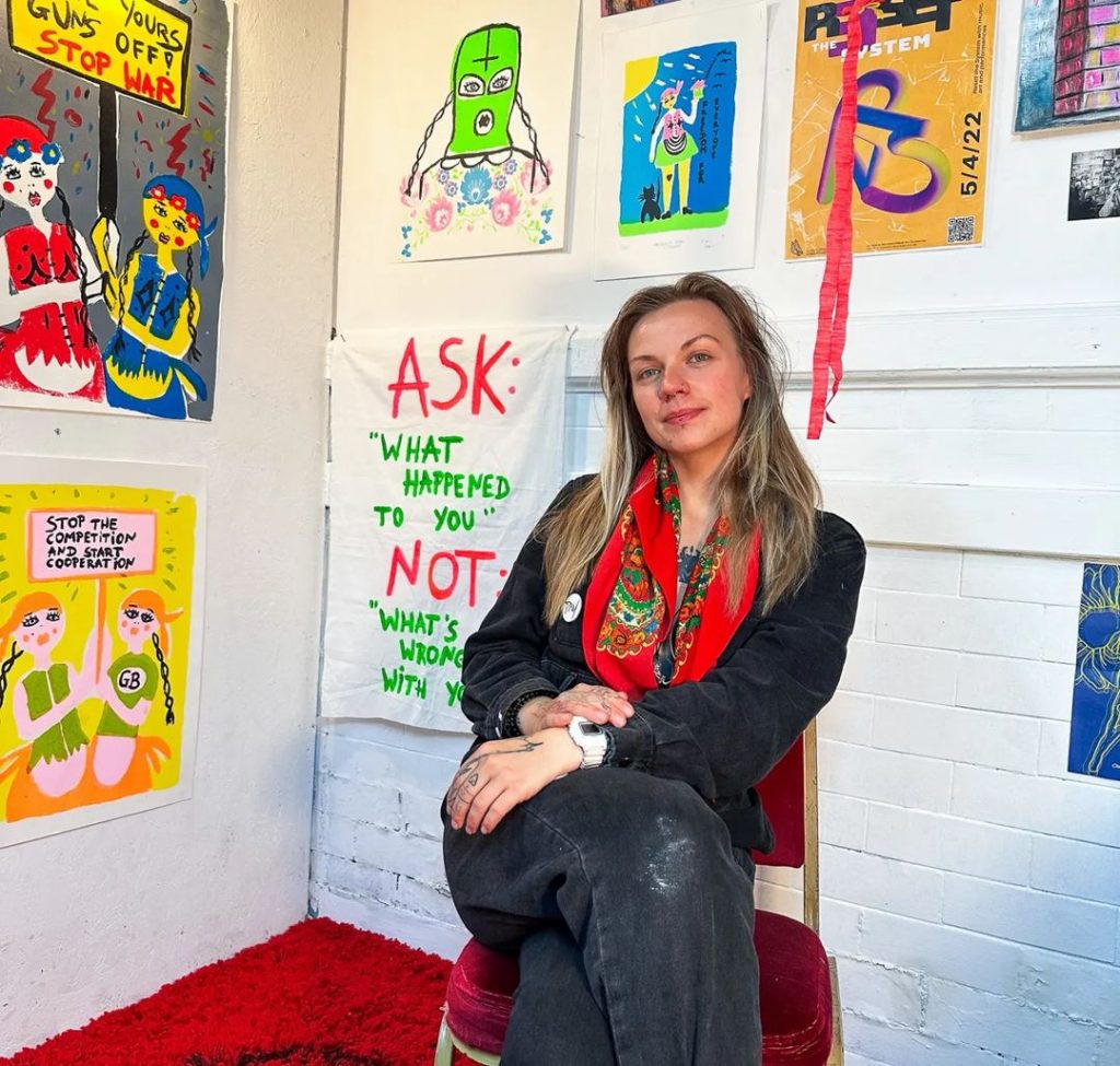 Graduate Scholar Maggie Stick in her studio with various 'artivist' works presented on the wall.