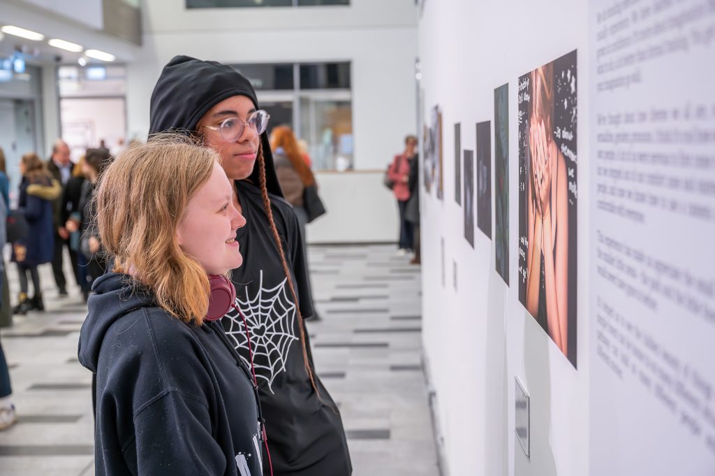 Two young people looking at their work installed as part of Craig Easton: Is Anybody Listening at the University of Salford, 2023.