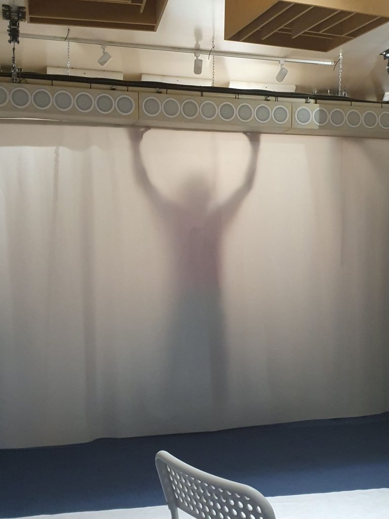 Team Assistant Sam Parker holding up and stood behind a projection fabric, he looks like ghost in the position of a Tusken Raider raising their sticks.
