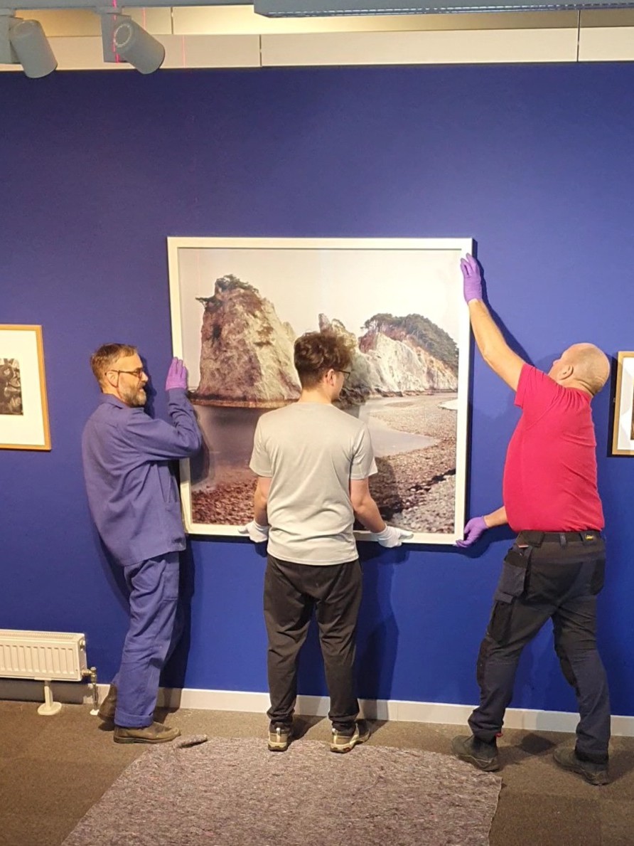 Team Assistant Sam Parker, Technician Craig Tattersall, and UoS Joiner Mr Fowley putting up one of Darren Almond's heavy framed photographs.