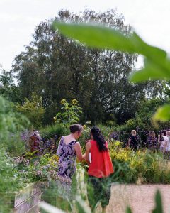 two women stand together chatting in a large garden on a sunny day