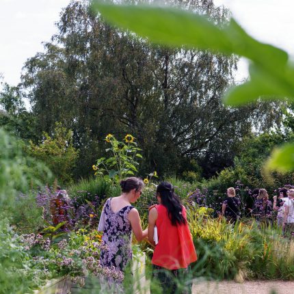 two women stand together chatting in a large garden on a sunny day
