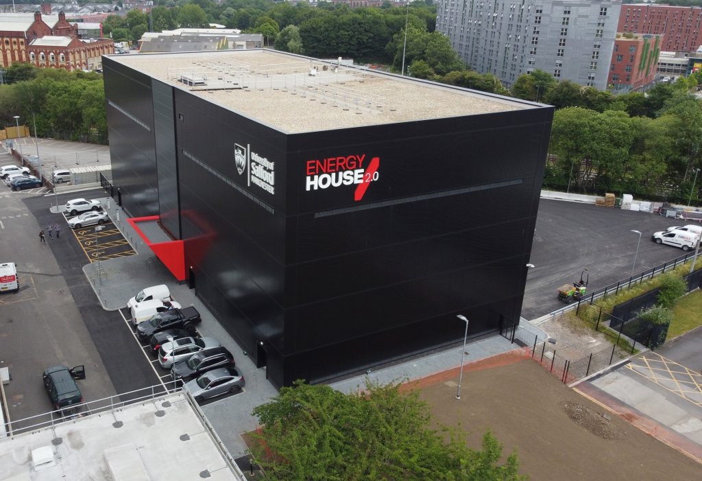 Energy House 2.0 building, a large black square shaped building with a white and red logo.