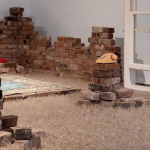 Bricks built in piles around room, with a rug and telephone in the centre.