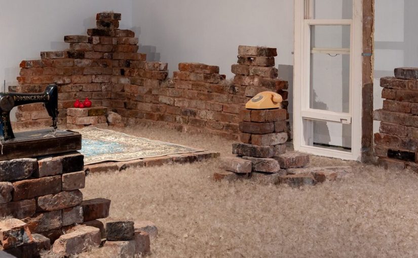 Bricks built in piles around room, with a rug and telephone in the centre.