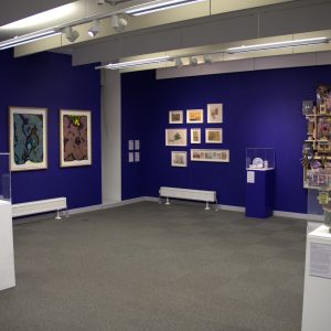 17 different artworks/artwork series' against a blue gallery wall and on top of plinths.